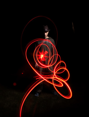 Abstraction, night portrait of a man in a hat in full growth with a red spiral of light in front of him, long exposure
