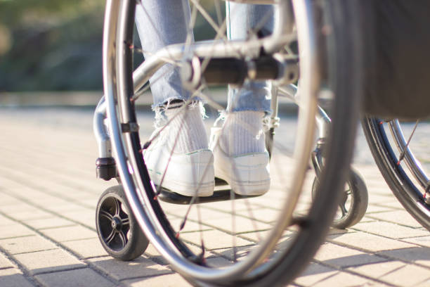 Person of unrecognizable gender and age sitting in wheelchair Person of unrecognizable gender and age sitting in wheelchair outdoors on sunny day. Close-up shot of thin legs in white sneakers and light blue jeans. Disability concept. eternity stock pictures, royalty-free photos & images