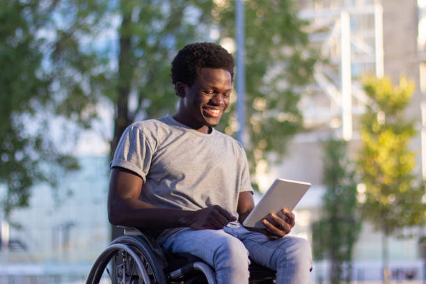 istock Young guy in wheelchair using his digital tablet in park 1443581486