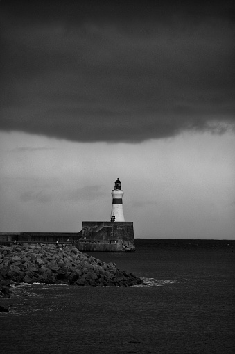 Fraserburgh harbour lighthouse in black & white taken as a storm was brewing with dark black clouds.