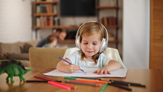 Adorable girl listening to music using headphones while drawing at home