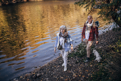 Man and woman, happy mature couple taking a walk by the river in nature on a beautiful autumn day.