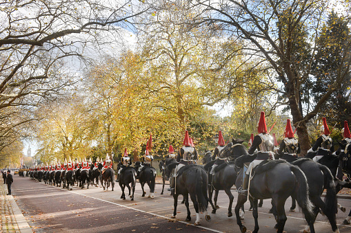 Horse guards ride down Constitution Hill in London towards a ceremonial under autumn leaves London, UK