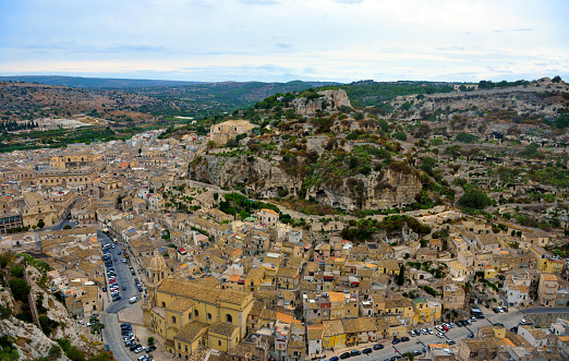 An idyllic cityscape of the old town of Matera, in southern Italy, known worldwide as 'Sassi di Matera' (Matera's Stones). At the center stands the majestic facade and the bell tower of the Duomo, or Cathedral of the Madonna della Bruna and of Sant'Eustachio, built in the Apulian Romanesque style in the 13th century. The ancient city of Matera, in the region of Basilicata, is one of the oldest urban settlements in the world, with a human presence that dates back to more than 9,000 years ago, in the Paleolithic period. The Matera settlement stands on two rocky limestone hills called 'Sassi' (Sasso Caveoso and Sasso Barisano), where the first human communities lived in the caves of the area. The rock cavities have served over the centuries as a primitive dwelling, foundations and material for the construction of houses, roads and beautiful churches, making Matera a unique city in the world. In 1993 the Sassi of Matera were declared a World Heritage Site by Unesco. Super wide angle image in 16:9 and High Definition format.