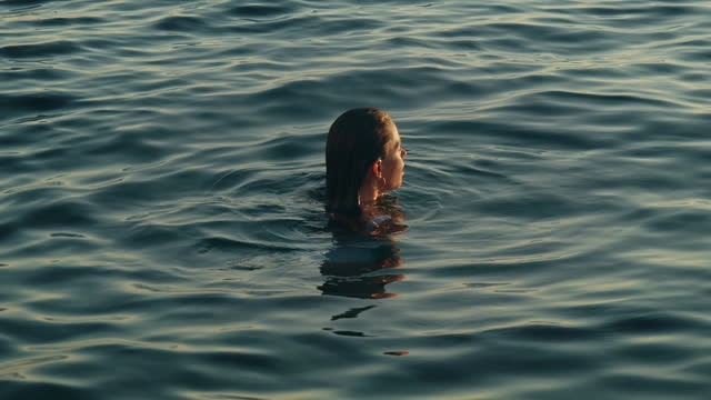 Woman relaxing in the sea suddenly immerses with the fantastic light of the sunset