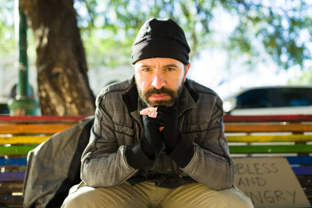 Miserable homeless man struggling living in the streets and looking hungry and sad sitting on the bench