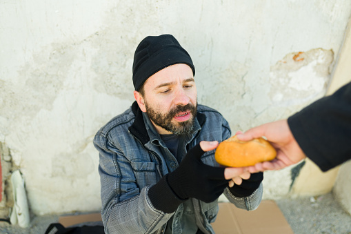 Sad hungry homeless man struggling to find food receiving a piece of bread from a man on the street