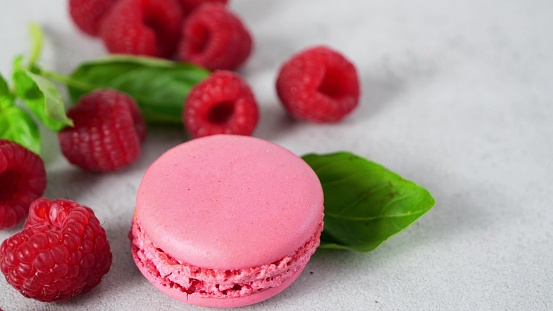 one pink macaron and a lot of red raspberries on a gray background close-up.