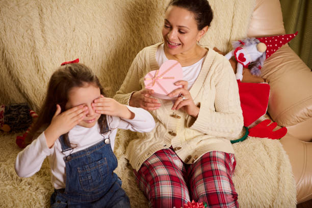 istock Lovely daughter closes her eyes with her hands, while her affectionate loving mother gives her cute Christmas present 1443606823