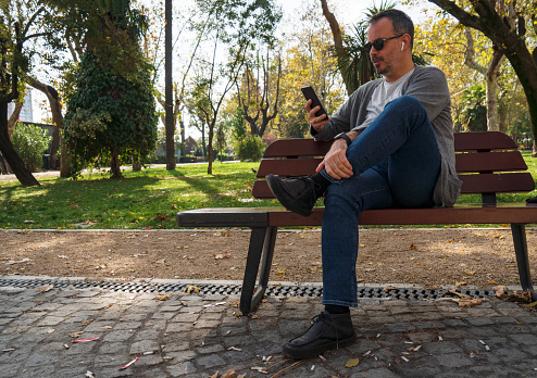 One man, sitting on park bench, using smart phone.