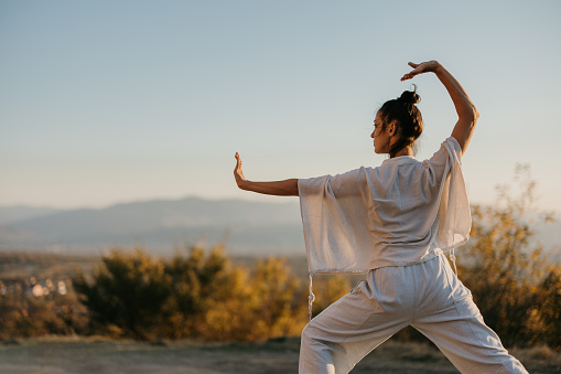 Woman practicing tai chi chuan on a meadow in sunset, in nature alone. Chinese management skill Qi's energy.