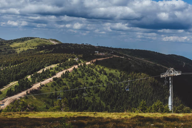 Scenic mountain landscape with summer ski resort in National park Kopaonik, Serbia. Panoramic view of green hills with ski trails, chair lift system and dense coniferous forest under blue cloudy sky.