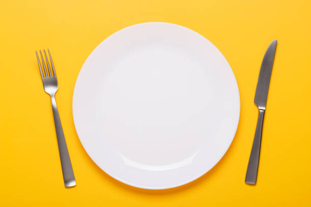 Clean empty white plate with knife and fork on yellow background stock photo