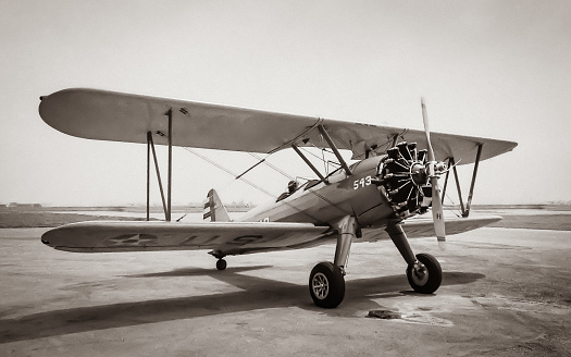 The airplane shown is a Stearman PT-17 biplane which was used by the US Army and US Navy to train pilots leading up to, and during, WWII.  The airplane was used in basic, or primary, training of new pilots.  The photo shows the full airplane from the right front quarter view.  One can see the silhouette of the pilot's head in the cockpit.  The engine is not running.  The markings on the lower wing can be seen and show US Army.  The photo is a classic sepia tone and evokes a clear feeling of history and nostalgia.