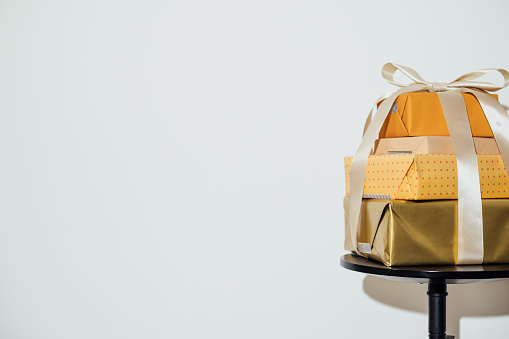 Xmas gift wrapped in gold wrapping paper with ribbon in front of white background.