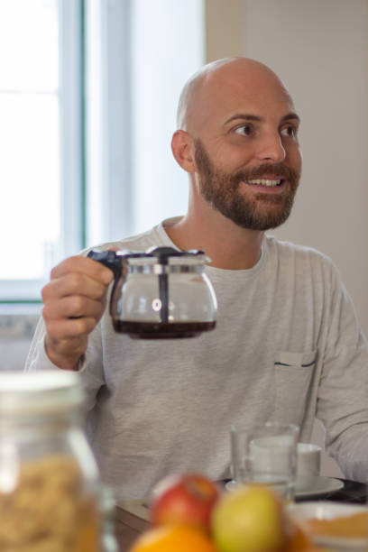 istock Cheerful man sitting at table and holding coffee pot 1443615003