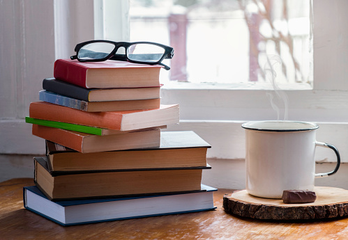 Hot coffee or tea, cocoa, chocolate cup on book and eyeglasses with copy space for text against the background of a bookshelf.