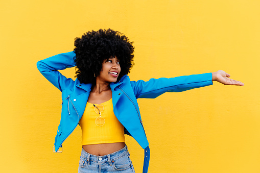 Beautiful young happy african woman with afro curly hairstyle strolling in the city - Cheerful black student portrait on colorful wall background