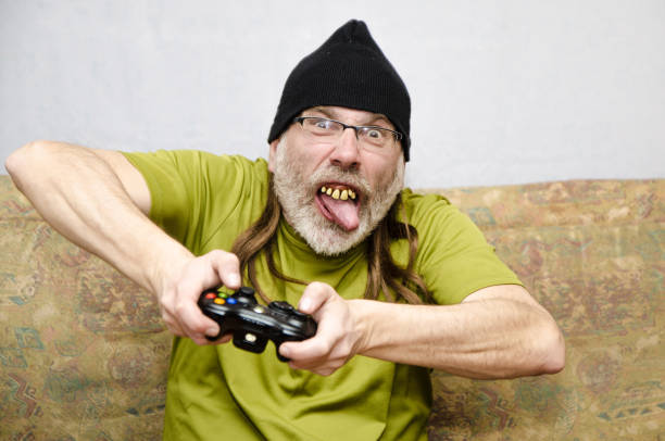 Ugly man with bad teeth (false dentures) at home during covid-19 pandemic lockdown playing video gamesHe wears a tuque over his long hair and a beard