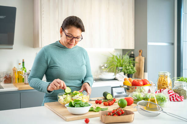 Mature woman preparing healthy vegetables salad Healthy eating: mature hispanic woman preparing healthy salad in domestic kitchen. High resolution 42Mp indoors digital capture taken with SONY A7rII and Zeiss Batis 40mm F2.0 CF lens weight loss stock pictures, royalty-free photos & images