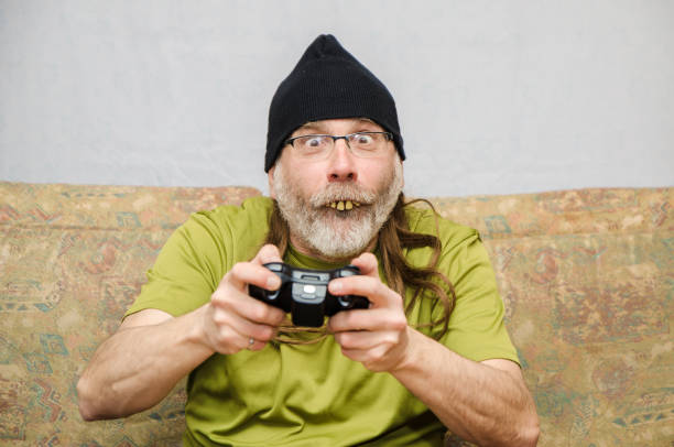 Ugly man with bad teeth (false dentures) at home during covid-19 pandemic lockdown playing video gamesHe wears a tuque over his long hair and a beard