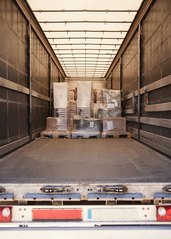 A partially full semi-truck seen from the rear doors containing pallets loaded with plastic covered cargo in the front section. Copy space