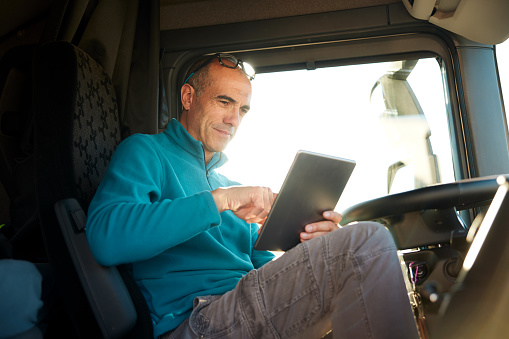 Mature male trucker reading off his digital tablet while sitting in the driver's seat. Close-up