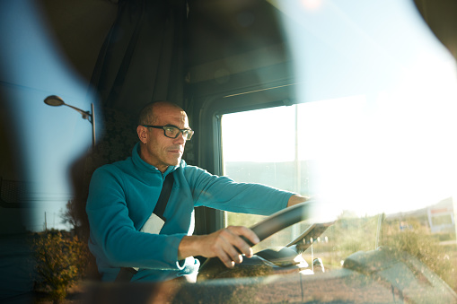 Concentrated mature adult male at the steering wheel travelling along the highway. Photographed through window, close up