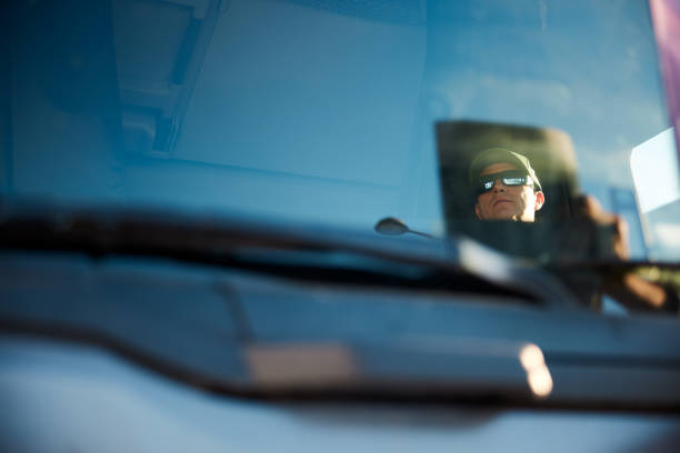 Headshot of truck driver wearing trucker hat and sunglasses taken through windshield. Copy space