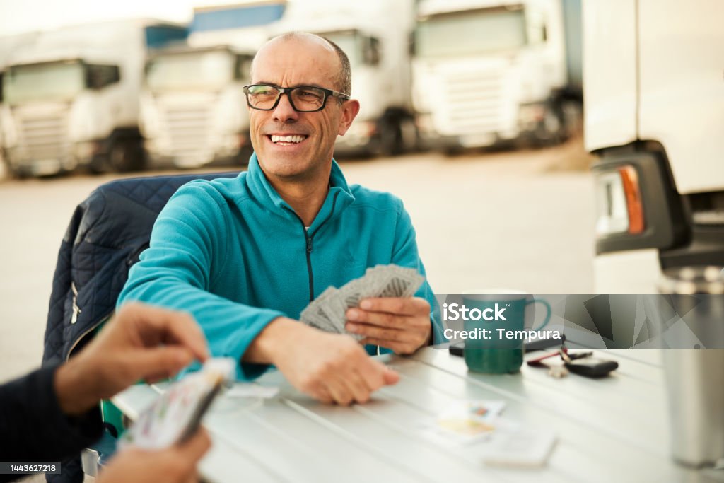 Game of cards for these truck drivers at a truck stop Two truckers, one partially viewed and the other with a big smile, outdoors playing cards at a rest area. Close-up Playing Card Stock Photo