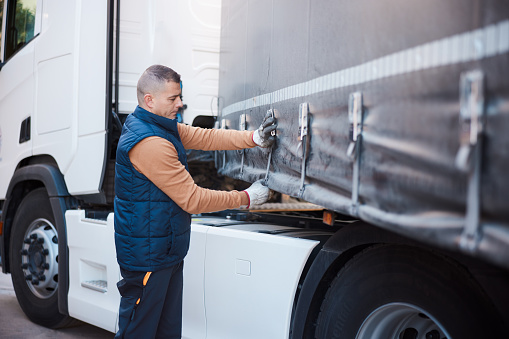 Mid adult male  trucker tightening tie down strap on left side of trailer. Three quarter length