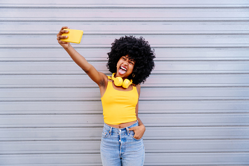 Beautiful young happy african woman with afro curly hairstyle strolling in the city - Cheerful black student portrait on colorful wall background