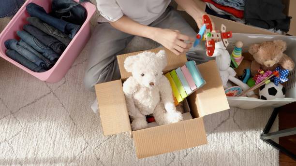 Boy preparing clothes and toys for charity donation. Teenage boy sorting and kid toys, clothes into boxes at home. Kid playing with old toys and packing them to cardboard box stock photo