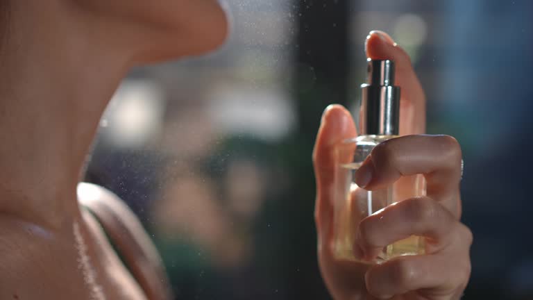 Close-up hand pressing cologne sprayer in slow motion spraying fragrance on female neck in slow motion. Side view closeup unrecognizable slim young Caucasian woman applying perfume.