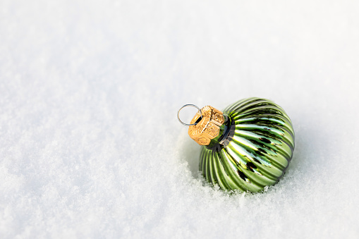 Glass green Christmas tree toy in the snow. Background on the theme of the new year. Copy Space