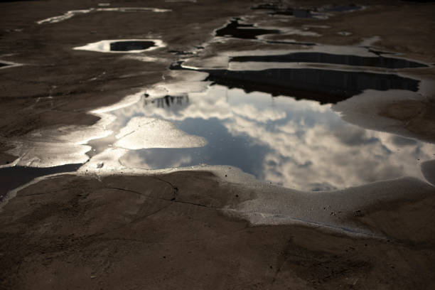 Large puddle on asphalt. Puddle after rain. Precipitation in city. Reflection of clouds in water.