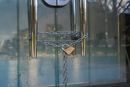 Close-up of a metal lock with a silver chain hanging on the handle of a glass door. A locked glass door. A closed place.