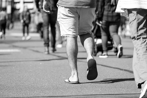 Black and white closeup male with Flip Flops walking in city, background with copy space, full frames horizontal composition