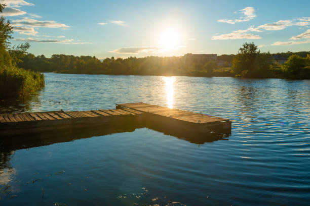 Wooden mooring bridge at water sunset with sun reflection on water