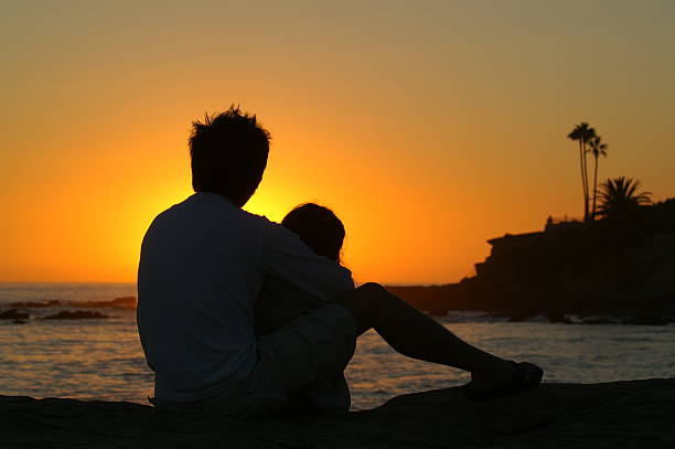 Couple cuddling as they watch the sun set stock photo