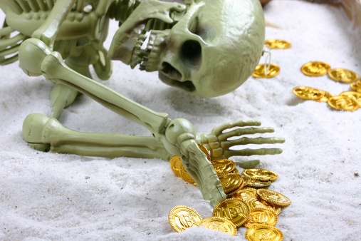 skeleton in the sand with gold coins, suggesting greed and illustrating the saying, 