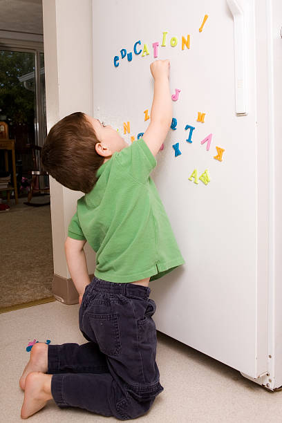 Fun on the Fridge Preschool boy playing with magnetic letters on the kitchen refrigerator. number magnet stock pictures, royalty-free photos & images