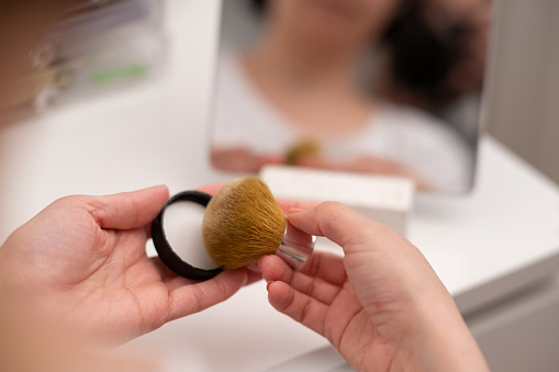 A woman’s hands while getting face powder to her kabuki brush.