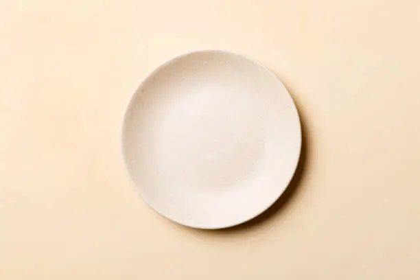 Photo of Top view of isolated of colored background empty round beige plate for food. Empty dish with space for your design