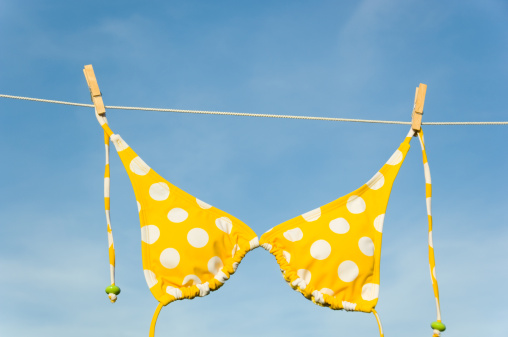 Yellow polka dot bikini hanging from a clothesline against blue sky
