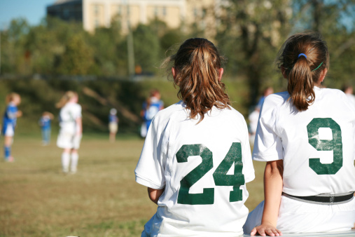 Two young female soccer players watching the game from the bench.