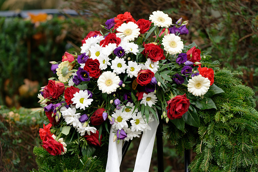 funeral wreath in a cemetery with colorful flowers and bow on a metal stand