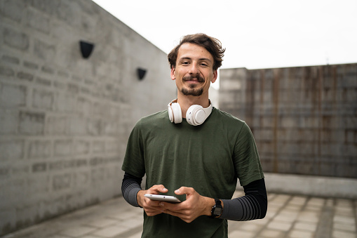 one man young adult caucasian male front view portrait of modern person with mustaches wear headphones looking to the camera real people copy space waist up standing confident outdoor use tablet