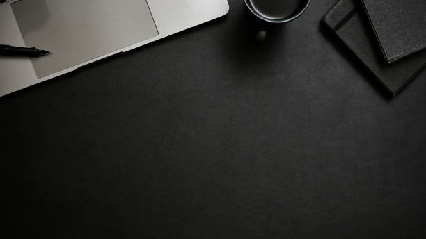 istock Stylish black workspace background with copy space, laptop, coffee cup and notepad. top view 1443721402