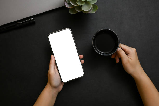 istock A female hands holding a smartphone mockup and a black coffee cup over modern black tabletop 1443721463